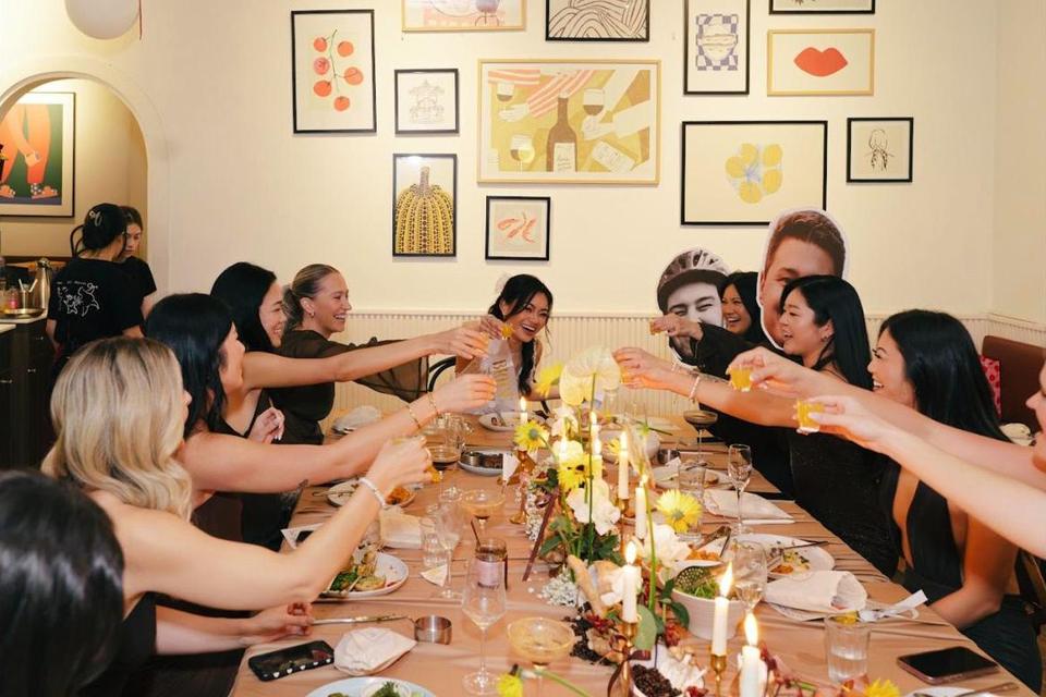 A long table of friends raising shot glasses