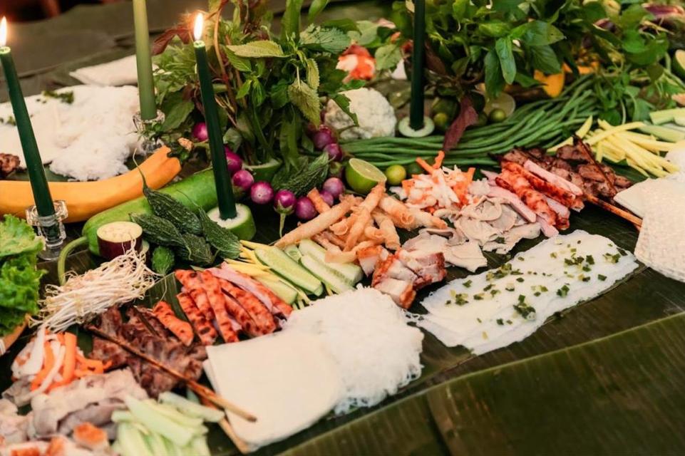 A candlelit grazing spread on banana leaves: herbs, grilled meats, rice paper and noodles